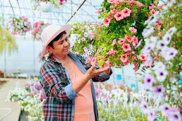 Femme fleuriste dans une chemise à carreaux vérifier soigneusement la qualité des fleurs cultivées en pot à effet de serre