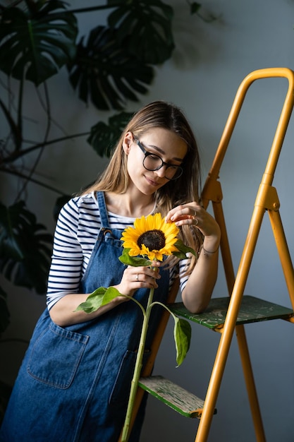 Photo une femme fleuriste entourée de plantes tropicales tenant du tournesol et touchant ses pétales