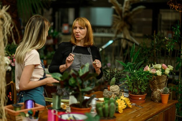 Femme fleuriste expérimentée aidant un jeune employé au fonctionnement de son entreprise