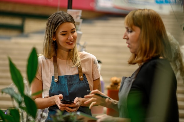 Femme fleuriste expérimentée aidant un jeune employé au fonctionnement de son entreprise