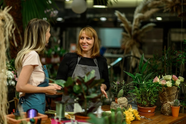 Femme fleuriste expérimentée aidant un jeune employé au fonctionnement de son entreprise