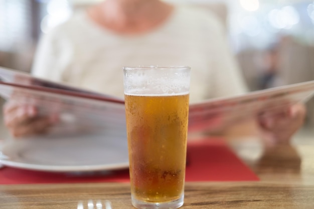 Femme floue assise au restaurant lisant le menu autour d'un verre de bière glacée