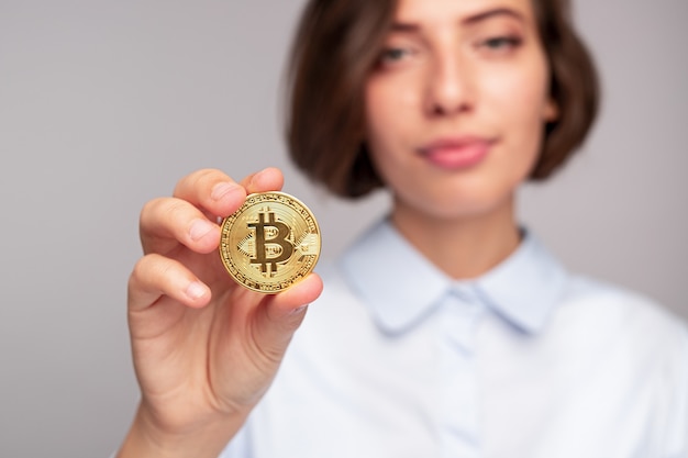 Femme floue démontrant le bitcoin doré à la caméra après avoir investi dans la crypto-monnaie sur fond gris