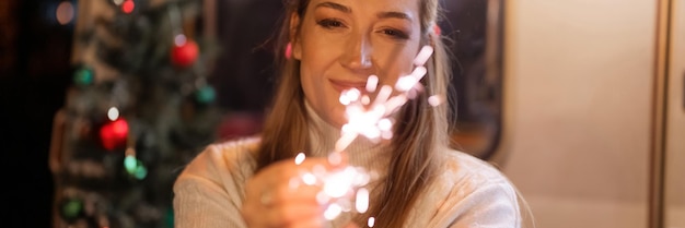 Femme floue en laine tricotée blanche chandail confortable mains tenant des cierges magiques bengale bâton de feu sur fond de caravane de camping en plein air le nouvel an et la nuit de la veille de noël bannière d'étincelles étincelantes