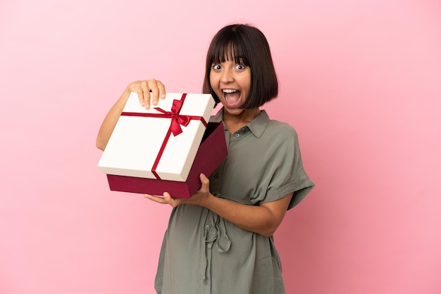 Femme sur fond isolé enceinte et tenant un cadeau avec une expression surprise