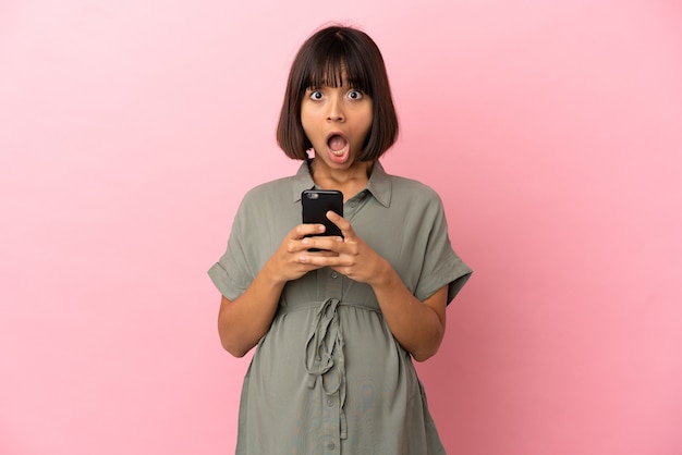 Femme sur fond isolé enceinte et utilisant un téléphone portable avec une expression surprise
