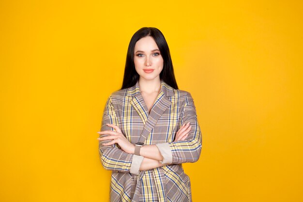 Une femme sur fond jaune, les mains croisées devant elle. Le concept de femme d'affaires ou de planification, de formation, de travail féminin.