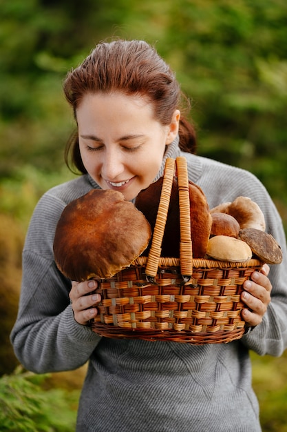 Une femme forestière renifle les champignons blancs et rouges frais collectés dans un panier d'aliments biologiques