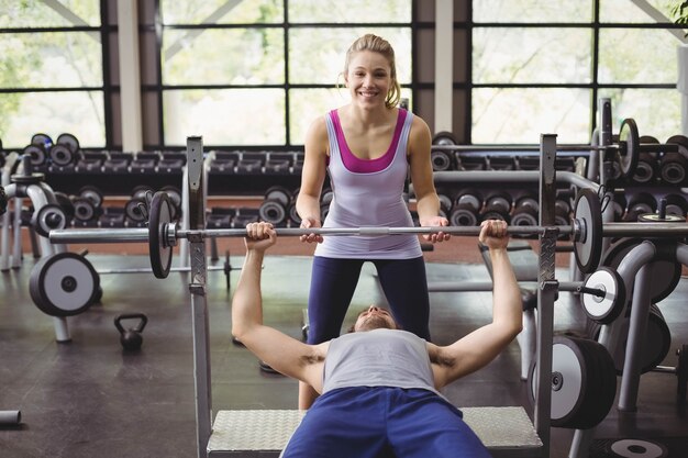 Femme de formateur aidant un homme sportif dans une salle de sport