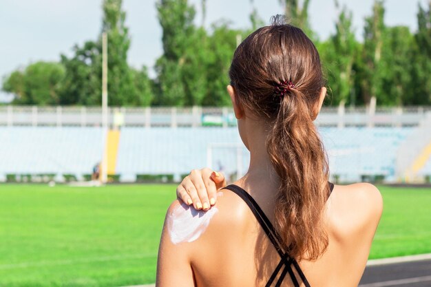 Une femme en forme applique un écran solaire sur son épaule avant de s'entraîner au stade Protégez votre peau pendant l'activité sportive