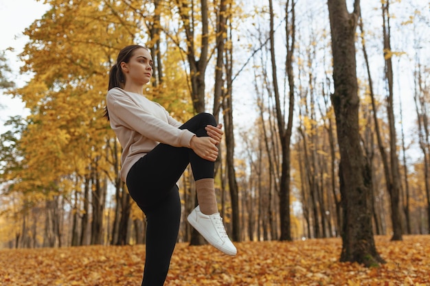femme en forme faisant de l'exercice et étirant la jambe levée pendant l'entraînement en automne dans la nature