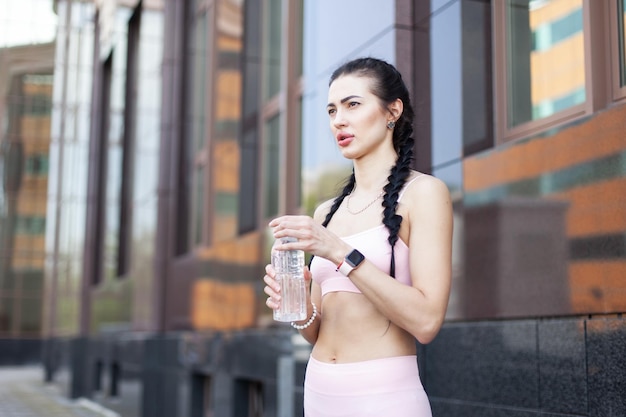 Une femme en forme fatiguée après une séance d'entraînement ou un jogging tenant une bouteille d'eau dans la ville