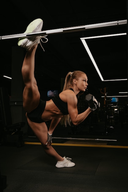 Une femme en forme avec de longs cheveux blonds fait une ficelle pendant des boucles de biceps d'haltères dans une salle de sport. Une fille s'étire.