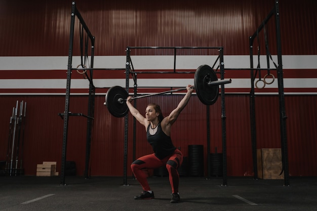 Femme forte soulevant des frais généraux d'haltères, faisant des exercices. Fit jeune femme soulevant des poids lourds au gymnase d'entraînement.