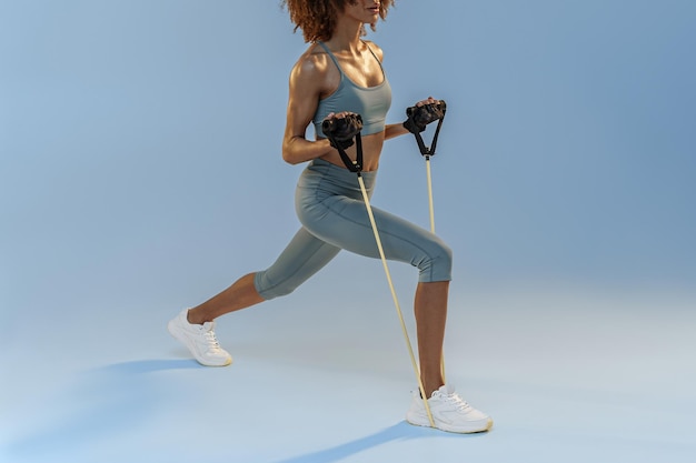 Une femme forte en vêtements de sport effectue des exercices de fitness avec une bande de résistance sur fond de studio