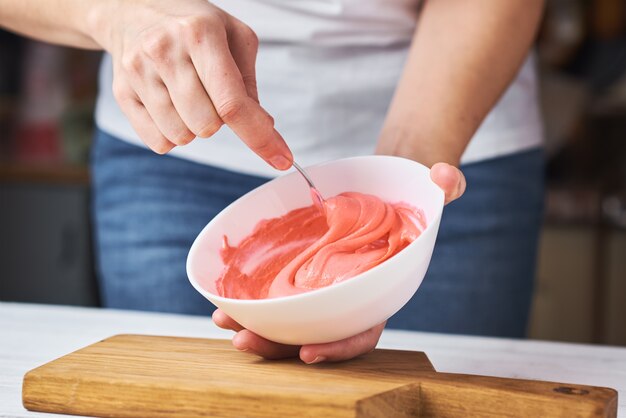 Femme fouettant la crème rouge pour décorer les cookies dans un bol sur la cuisine, gros plan