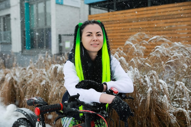 Une femme en foulard vert et noir assise sur un vélo dans la neige