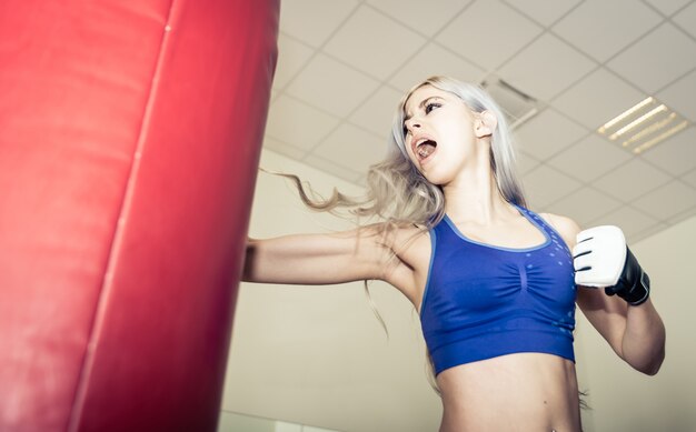 Femme frappe le sac lourd de boxe dans la salle de gym