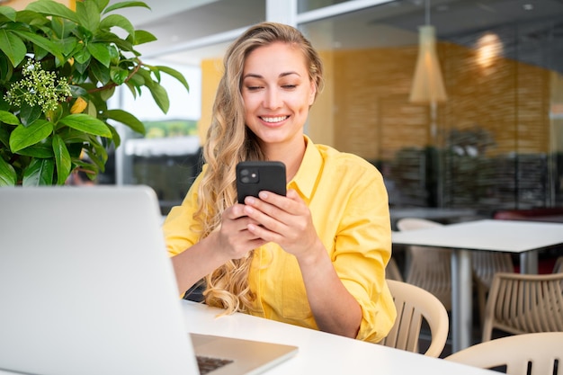 Une femme freelance souriante utilisant un smartphone dans un café en plein air