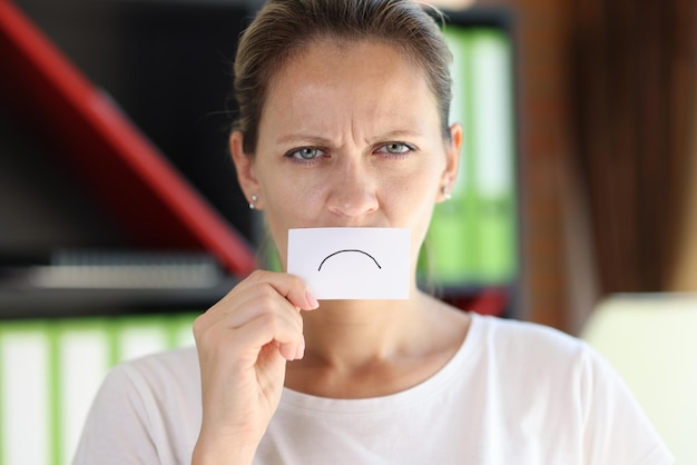 Une femme frustrée a couvert sa bouche de papier avec une émoticône triste