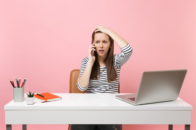 Une femme frustrée s'accrochant à la tête parlant sur un téléphone portable reçoit de mauvaises nouvelles s'assoit travailler sur un projet au bureau avec un ordinateur portable
