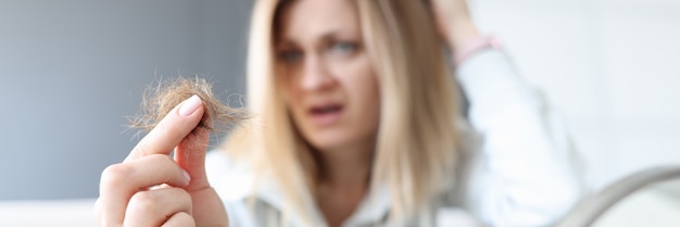 Une femme frustrée tient un chignon de ses cheveux dans son concept de perte de cheveux à la main