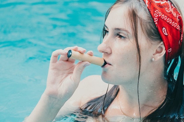 Femme fumant avec une cigarette électronique. Jeune femme fumant une cigarette électronique dans une piscine extérieure