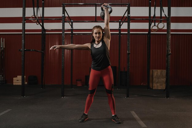 Femme gaie forte avec un corps musclé faisant de l'exercice avec un kettlebell pendant l'entraînement