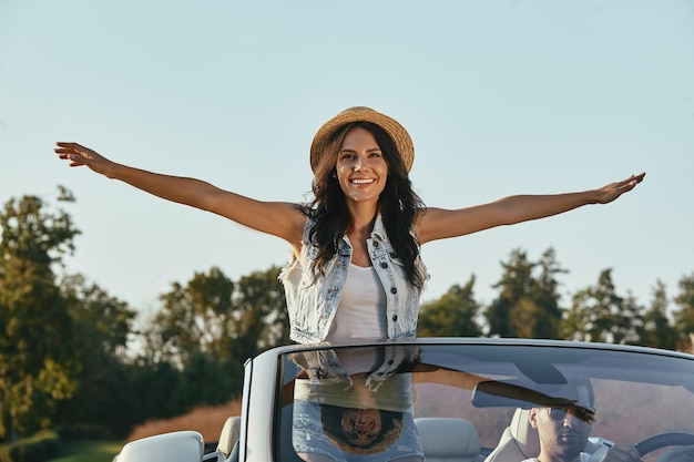 Femme gaie levant les mains pendant que l'homme conduit un cabriolet