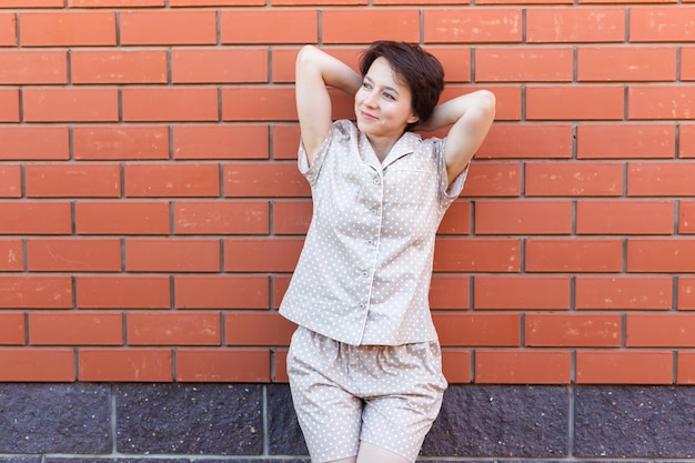 Femme gaie à la maison porter un pyjama en plein air mur de briques émotions d'arrière-plan copier l'espace et la place vide pour le texte vêtements de nuit et concept de vêtements d'intérieur