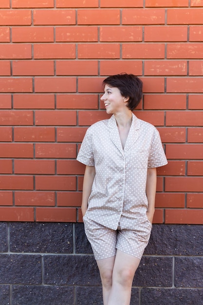 Femme gaie à la maison porter un pyjama en plein air mur de briques fond émotions vêtements de nuit et concept de vêtements d'intérieur