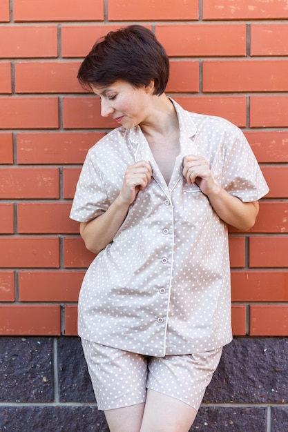 Femme gaie à la maison porter un pyjama en plein air mur de briques fond émotions vêtements de nuit et concept de vêtements d'intérieur