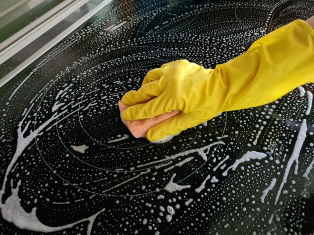 Femme en gants de caoutchouc jaune nettoie la cuisinière à induction de cuisine avec une éponge de nettoyage