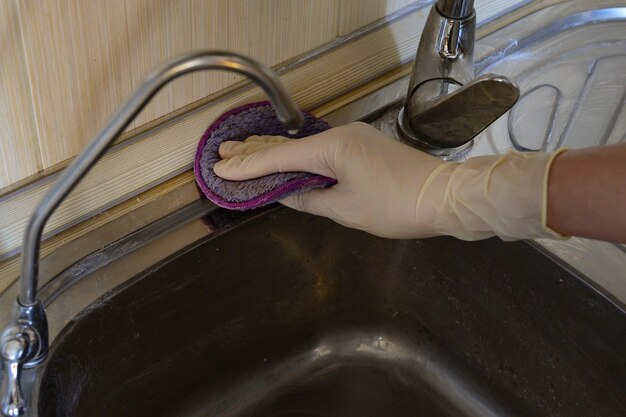 Une femme en gants de caoutchouc nettoie l'évier avec du détergent.