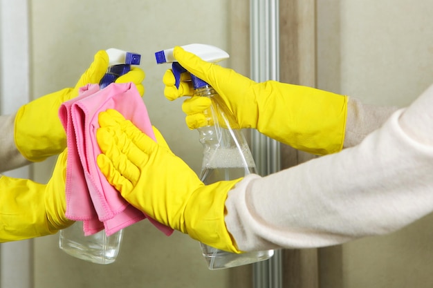 Une femme en gants essuie le miroir avec des détergents en gros plan