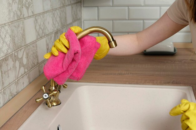 Femme en gants essuie le robinet avec un chiffon Femme nettoie la cuisine