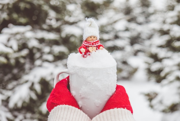 Photo une femme en gants rouges tient la tasse avec de la neige et un joli jouet de noël à l'intérieur.