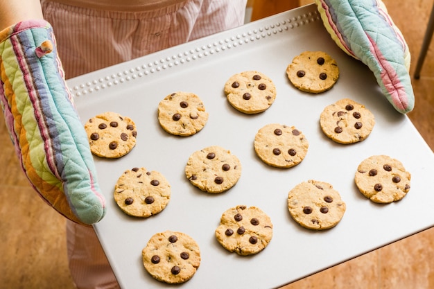 Femme avec des gants tenant un plateau de biscuits au four