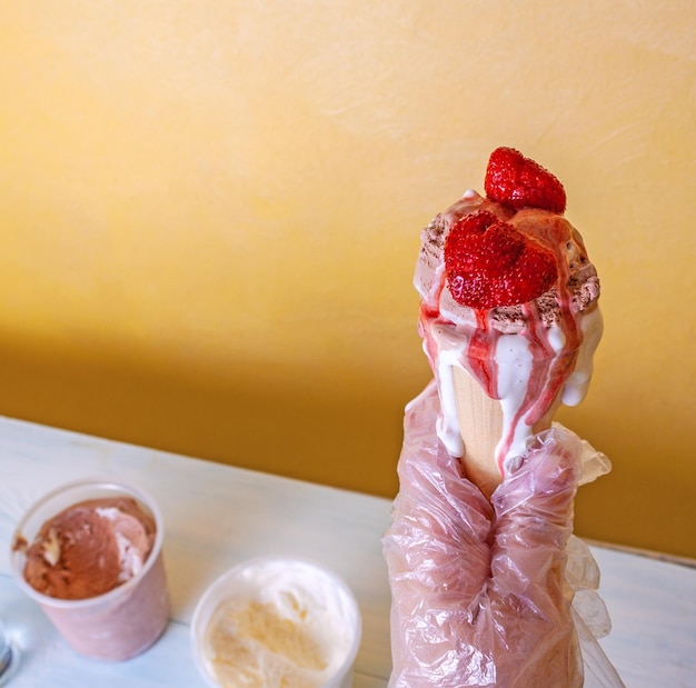 Une femme en gants tient une crème glacée rafraîchissante au chocolat et à la vanille avec des fraises dans un cône de gaufres