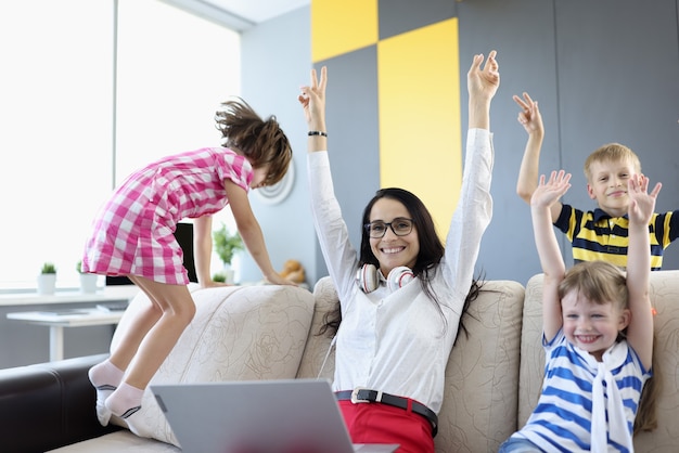 Femme, garçon et deux filles sont assis sur un canapé et rient joyeusement et lèvent les mains