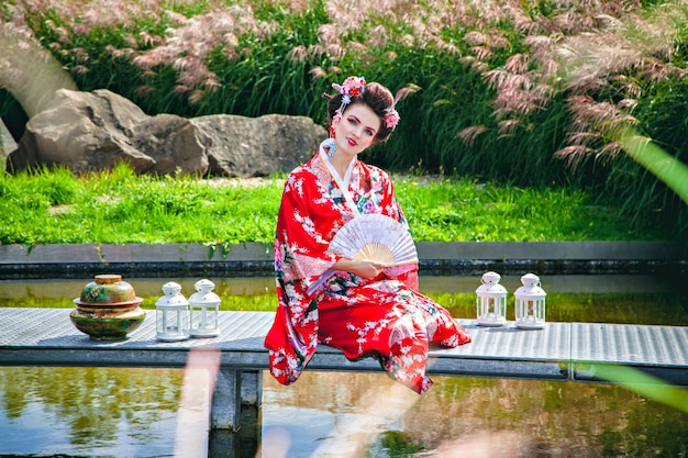 Femme Geisha japonaise avec maquillage fantaisie dans le jardin avec un ventilateur