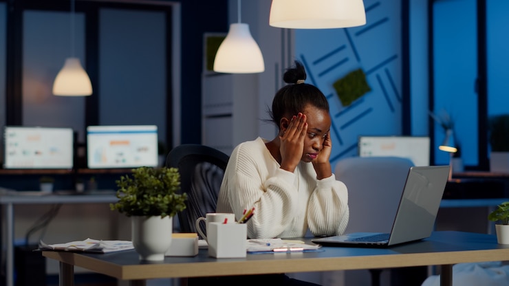 Photo femme gestionnaire africaine surmenée massant la tête alors qu'elle était assise sur le lieu de travail dans un bureau de démarrage faisant des heures supplémentaires sur un ordinateur portable. femme d'affaires tendue épuisée respectant la date limite face à la migraine