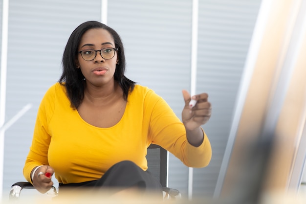 Une femme gestionnaire afro-américaine pointant une présentation de tableau blanc à divers employés lors d'une réunion dans un bureau moderne