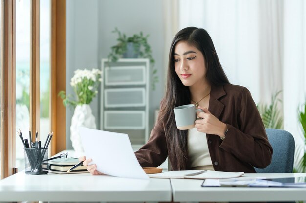 Photo une femme gestionnaire attrayante boit une tasse de café et lit des rapports au bureau