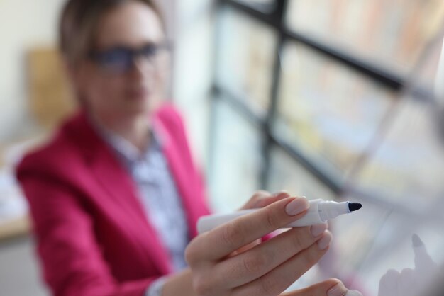 Femme gestionnaire dessinant à bord avec marqueur sélectionné focus enseignant écrit à bord à l'école