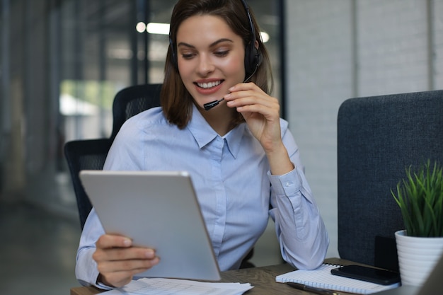 Une femme gestionnaire joyeuse assise au bureau et effectuant des tâches d'entreprise à l'aide d'une connexion sans fil sur des gadgets numériques.