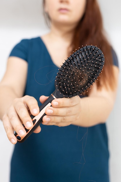 Photo femme gingembre aux cheveux longs recadrée en t-shirt bleu présentant un peigne à cheveux avec des cheveux à l'appareil photo montrant hai