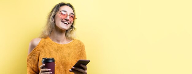 Femme glamour à lunettes dans un pull orange avec un verre de café sur fond jaune