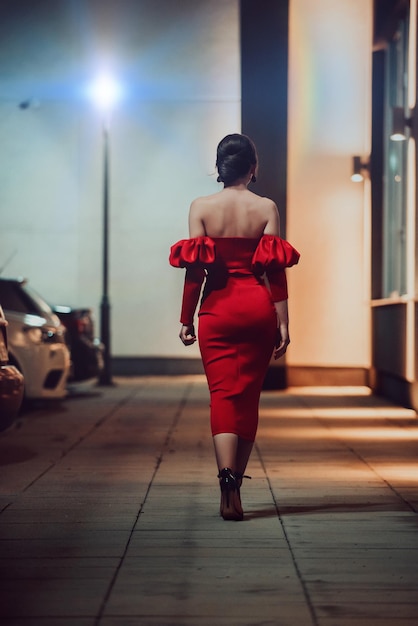 Une femme glamour en robe rouge posant dans la ville