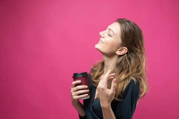 Femme glamour vêtue d'une robe bleu foncé avec un verre de café sur fond rose